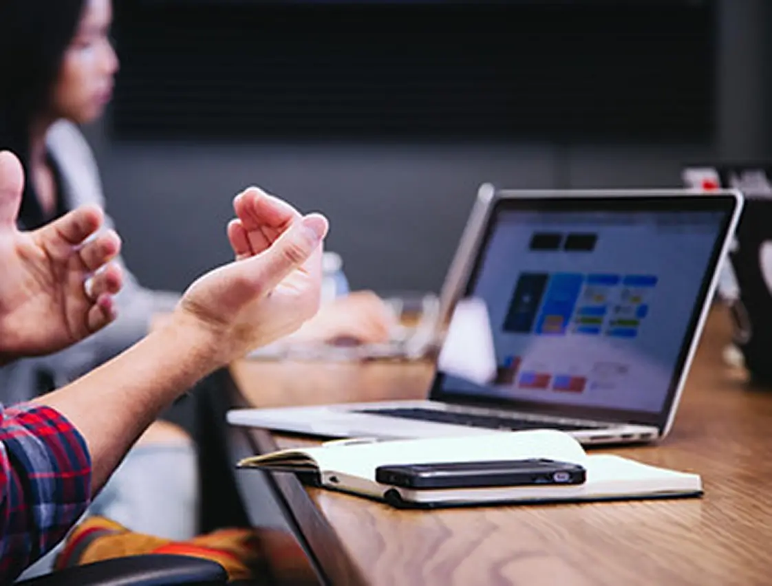 Team meeting around a laptop showing a design, with hands gesturing mid-discussion